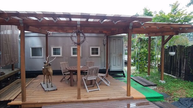 A covered patio with a wooden table and chairs, a deer statue, and a pergola structure. - Country House Morning Salad (Fujikawaguchiko)