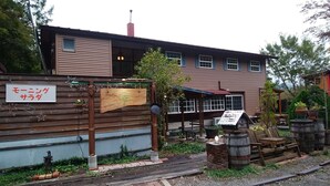 A rustic building with a wooden signboard, a small outdoor seating area, and a sign indicating a restaurant. - Country House Morning Salad (Fujikawaguchiko)