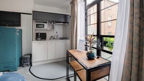 A compact kitchen with a microwave, stove, and cabinets, a teal wardrobe, and a window with curtains. - Garden facing studio with Juliet balcony. Walk to seafront, shops & restaurants. (Portsmouth)