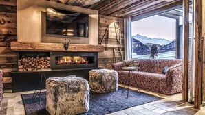 Un salon chaleureux avec une cheminée, un grand téléviseur fixé au mur et une vue sur des montagnes enneigées.