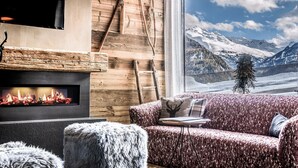 Un salon chaleureux avec une cheminée, un mur en bois, un canapé et une vue sur des montagnes enneigées.