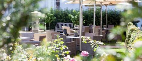 An outdoor patio with wicker furniture, umbrellas, and a garden with flowers.
