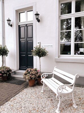 En hvid bænk foran en bygning med en sort dør, plantekasser og et skilt, der siger "Ferienwohnung".