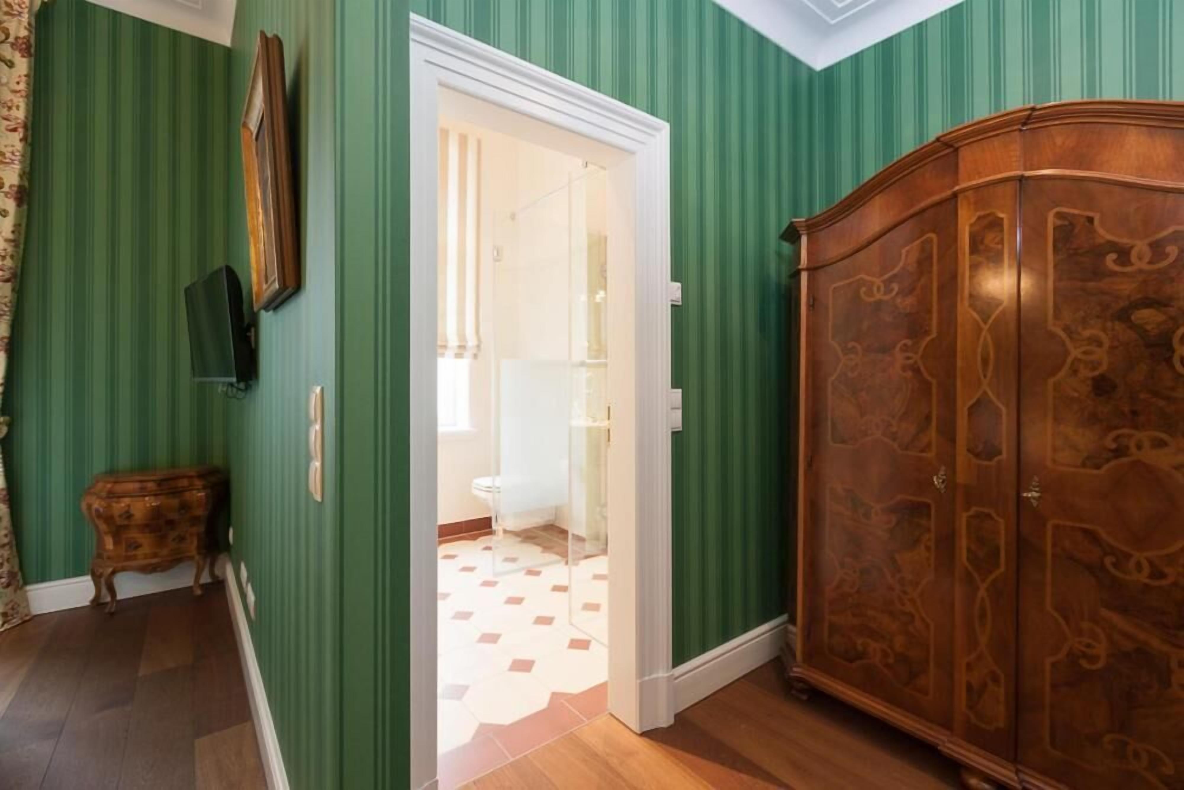 Une pièce aux murs verts, avec une armoire en bois, une petite commode en bois et une porte donnant sur une salle de bain.