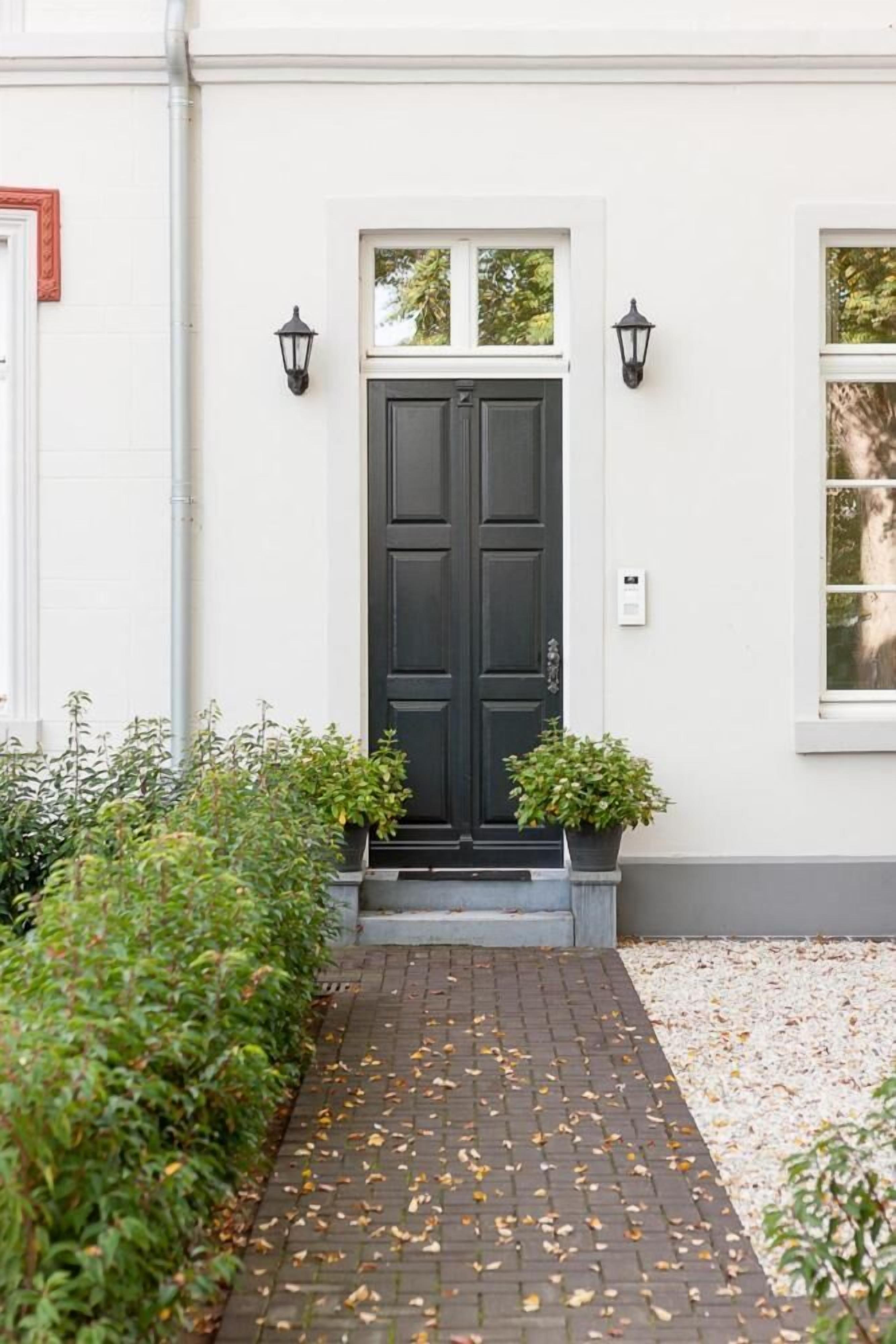 A white building with a black double door, two black wall-mounted lights, and a small potted plant beside the door.
