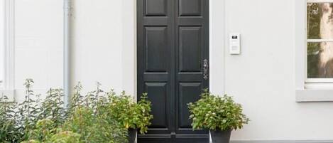 A white building with a black double door, two black wall-mounted lights, and a small potted plant beside the door.
