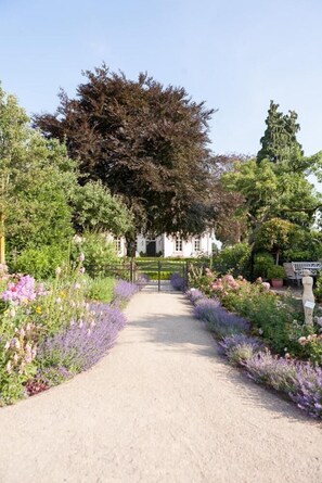 A garden pathway leading to a white building with a black gate. - Exklusive Ferienzimmer Gut Heidefeld (Bocholt)