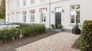 A white building with a black door, a statue, and a gravel driveway. - Exklusive Ferienzimmer Gut Heidefeld (Bocholt)