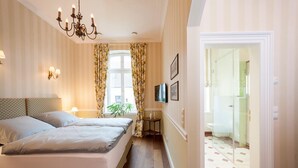 A hotel room with two beds, a chandelier, a small table with a plant, and a bathroom visible through a glass door. - Exklusive Ferienzimmer Gut Heidefeld (Bocholt)