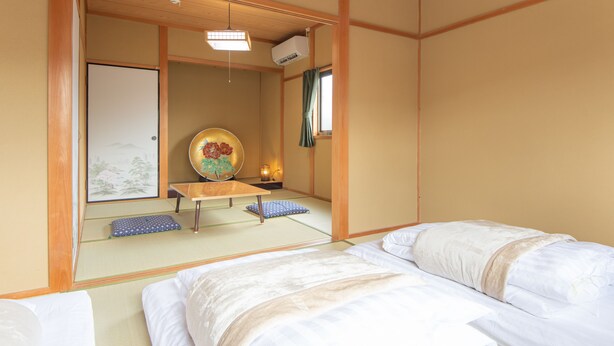 A traditional Japanese room with tatami flooring, a futon bed, a shoji screen, and a painting on the wall. - The EXP Yachiyo (Uda)