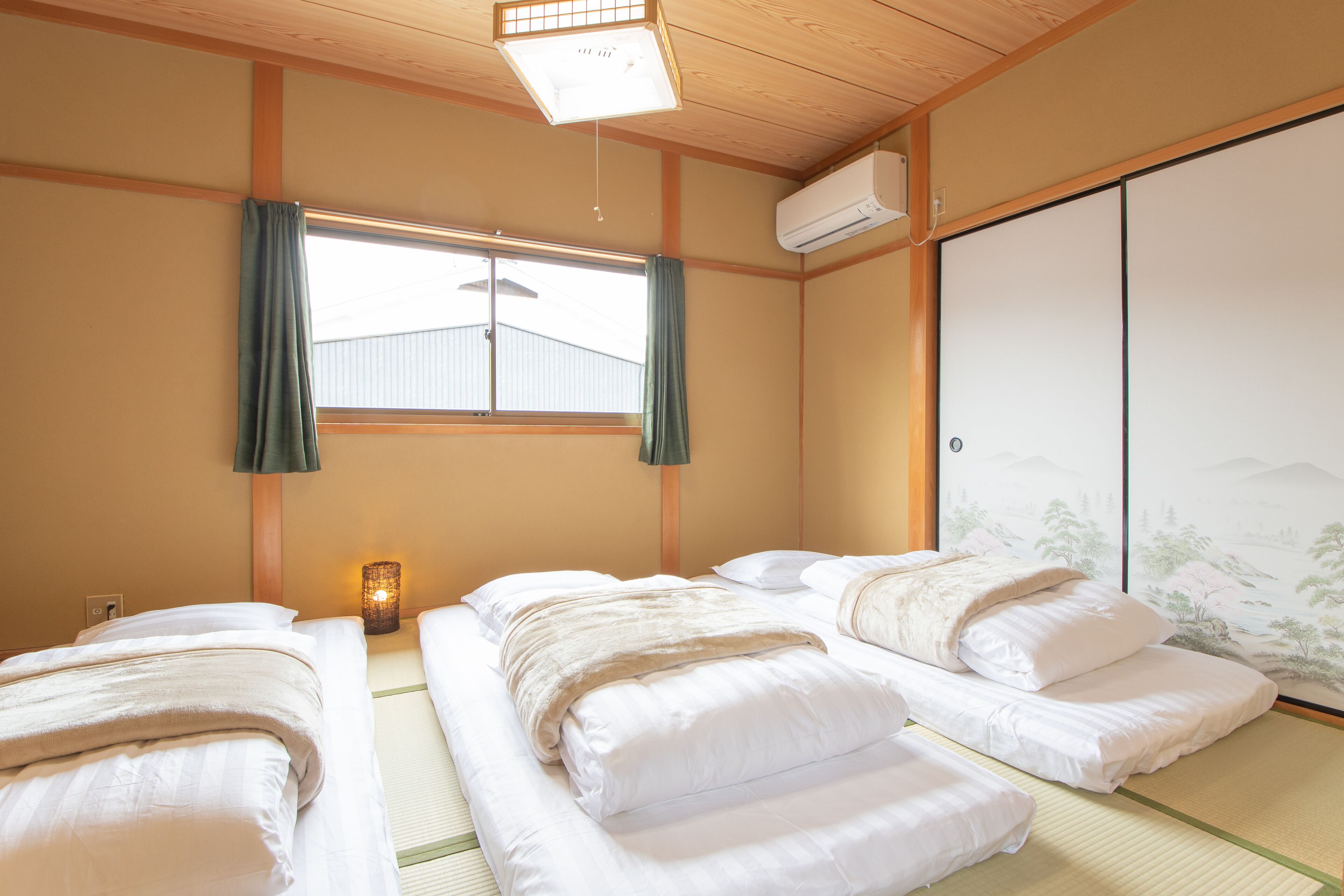 A traditional Japanese room with tatami flooring, two beds with white bedding, a shoji screen, and a hanging lantern.