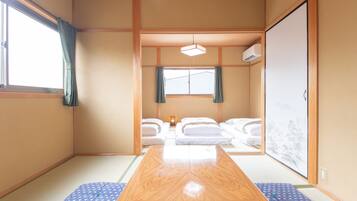 A traditional Japanese room with tatami flooring, a wooden table, futons, and a sliding door with a view of a mountain.