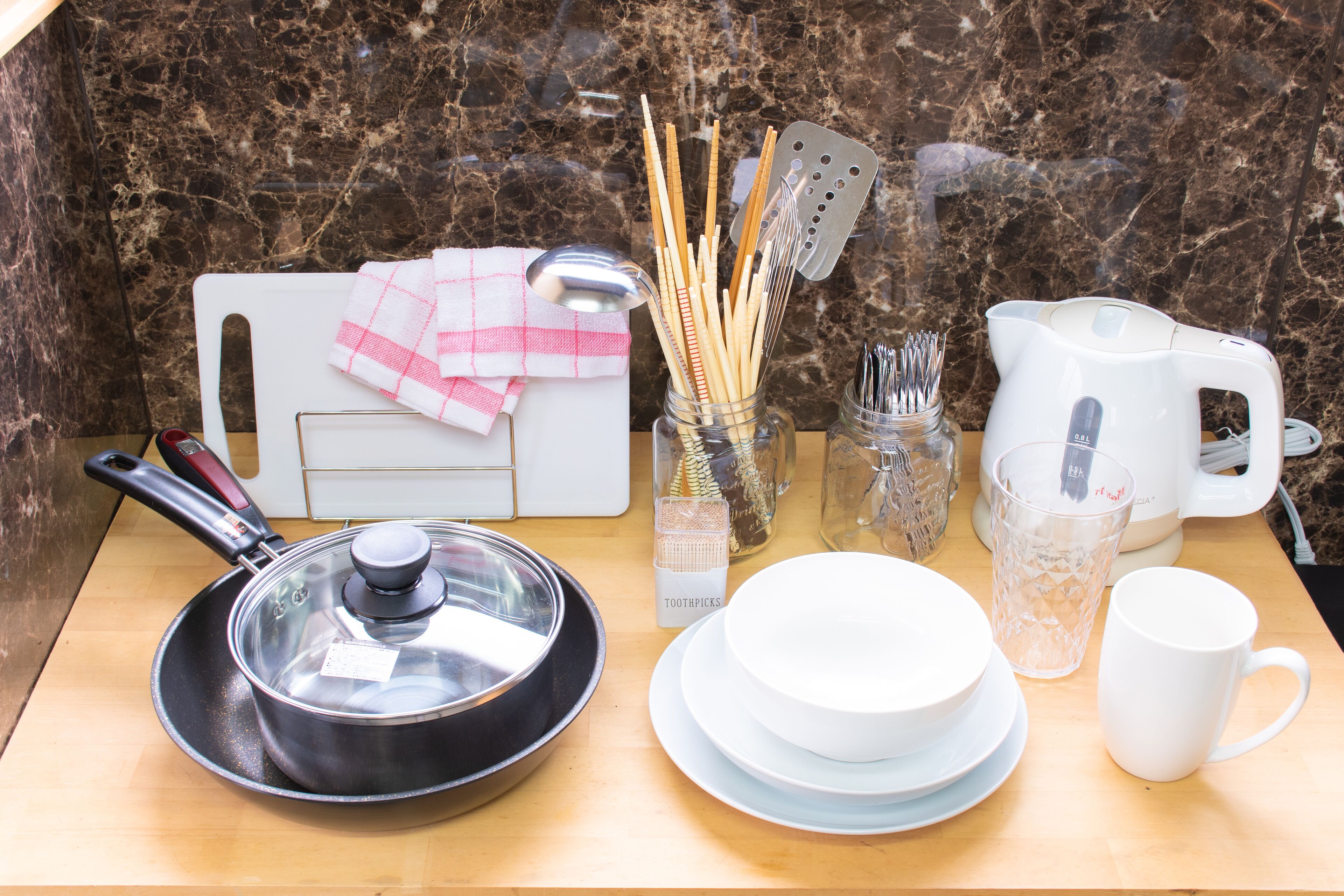 A kitchen counter with a frying pan, a kettle, a cup, a bowl, a knife block, and a jar of utensils.