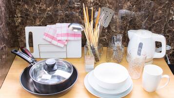 A kitchen counter with a frying pan, a kettle, a cup, a bowl, a knife block, and a jar of utensils.