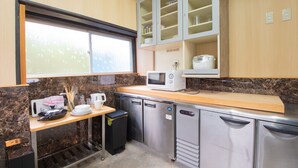 A compact kitchen with a microwave, a small refrigerator, and a sink. There is a window above the sink, and cabinets above the countertop. - The EXP Yachiyo (Uda)