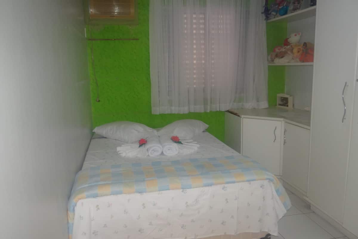 A small, neatly made bed with a floral-patterned bedspread, a white headboard, and a green wall.