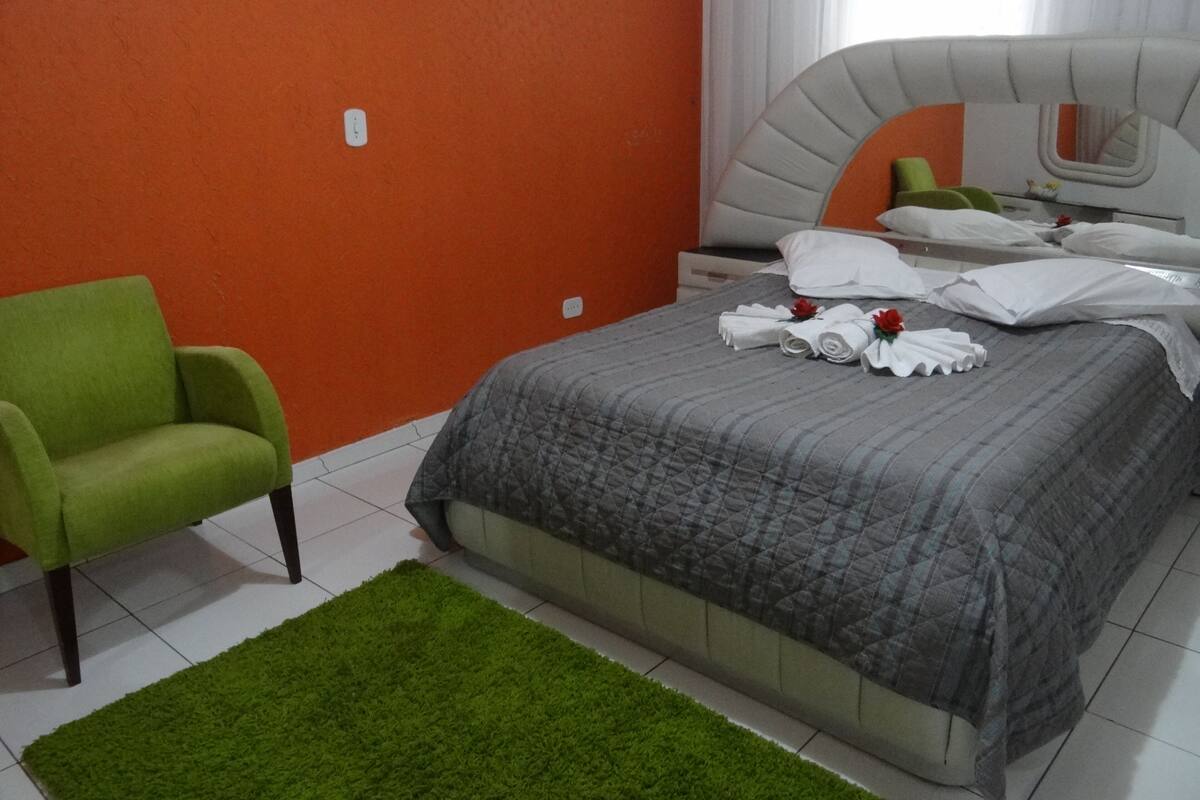 A hotel room with a bed, a green armchair, and a green rug.