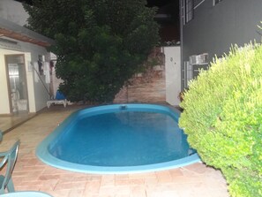 A swimming pool with a tiled deck, surrounded by a hedge and a stone wall. - Casa Temporada Jardim Iguaçu (Foz do Iguaçu)