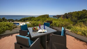 A patio with a table set for two, featuring a book, a fruit bowl, and wine glasses. - Villa Quinta da Marinha (Carvoeiro)