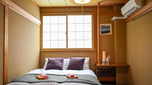 Habitación de hotel con cama, ventana, mesita de noche con botellas y un cuadro en la pared.
