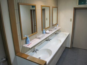 A long, white bathroom with two sinks, a mirror, and a door. - Asuka Lodge (Hakuba)