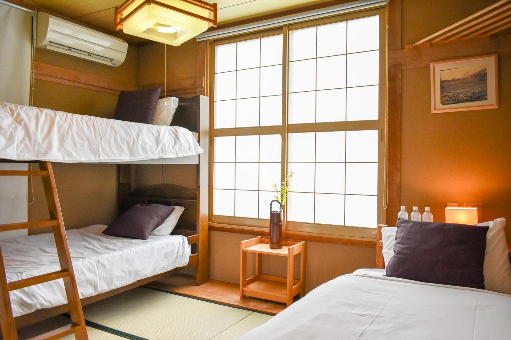 A traditional Japanese-style room with bunk beds, a small wooden table, and a window with a view.