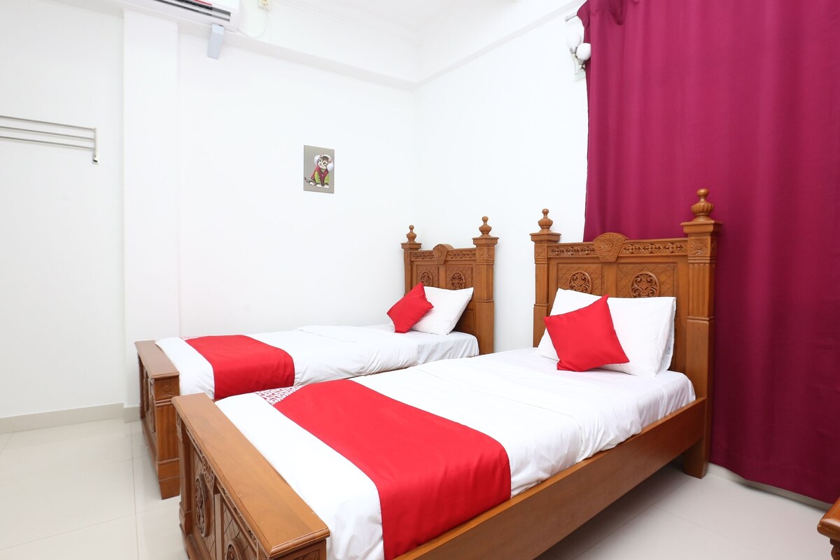 A room with two wooden beds, each with a red and white bedspread, and a red curtain on the right.