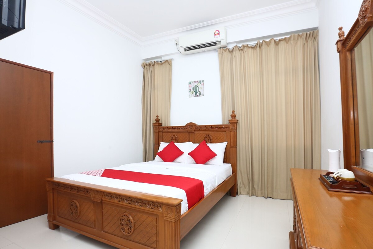 A hotel room with a wooden bed, a wooden desk, a wardrobe, and an air conditioning unit.