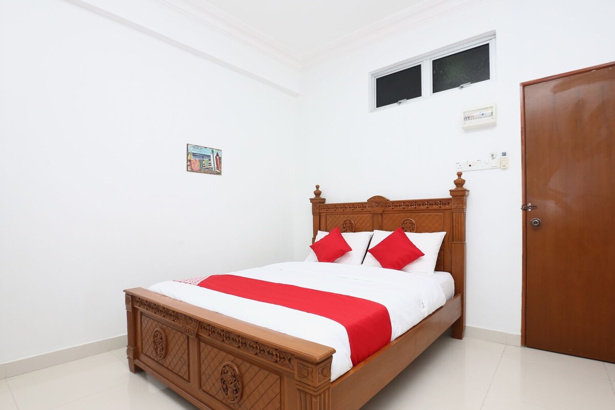 A neatly made bed with a wooden headboard, a red and white bedspread, and matching pillows.