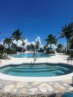 A pool area with multiple swimming pools, palm trees, and lounge chairs. - Beachfront- BREEZY POINT CONDO. "Newly Furnished"! (Wheeland Settlement)