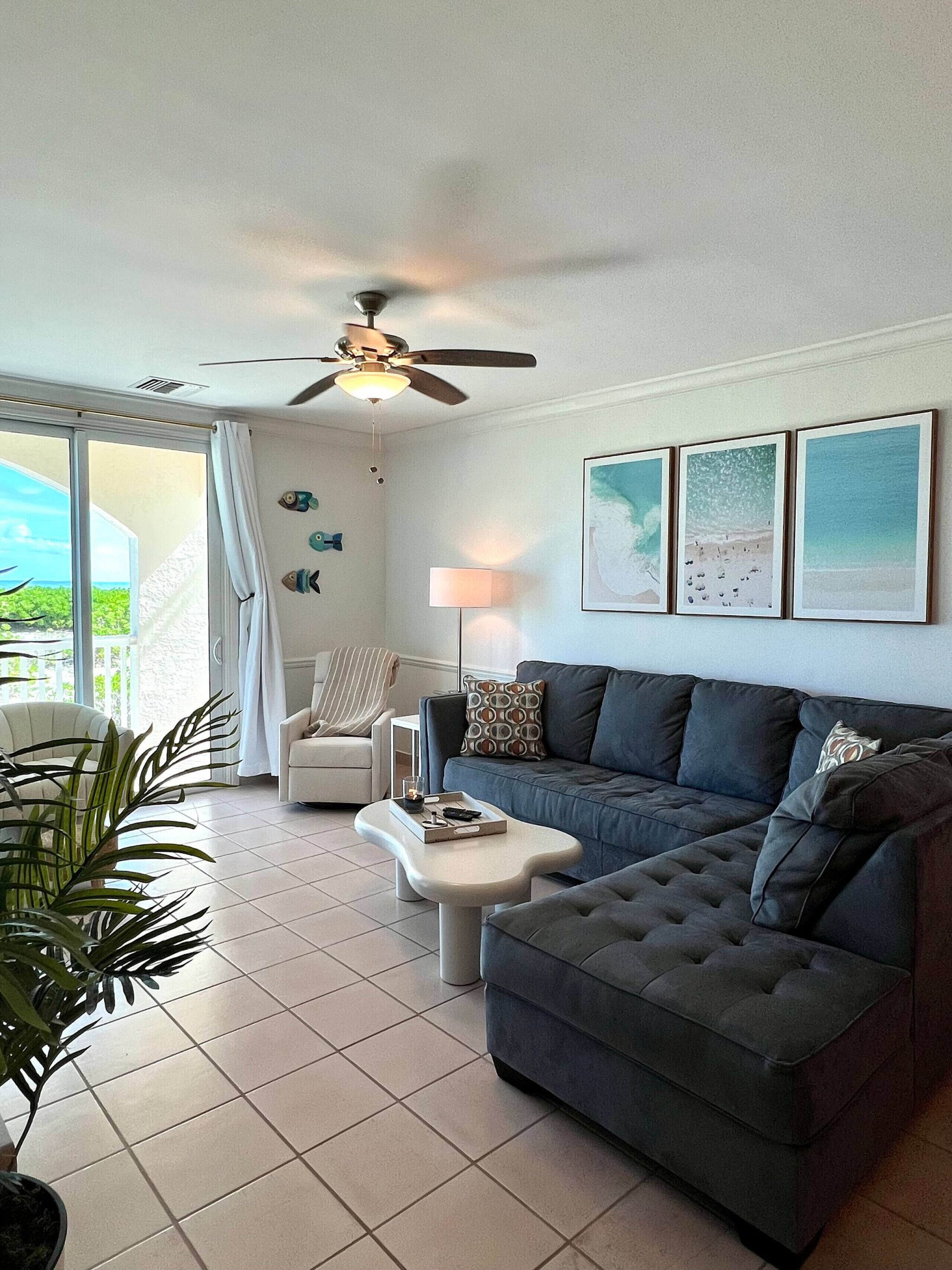 A living room with a sofa, a coffee table, a ceiling fan, and a view through a sliding glass door.