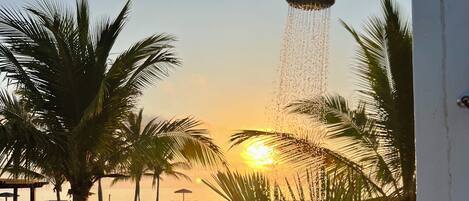 A sunset view from a balcony with a water feature, palm trees, and a wooden deck.