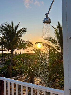 A sunset view from a balcony with a water feature, palm trees, and a wooden deck.