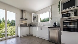 Une cuisine moderne avec des meubles blancs, des appareils en acier inoxydable et une grande fenêtre donnant sur un paysage verdoyant.