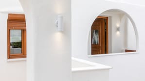 A white exterior wall with a wooden door and window, and a white pillar with a light fixture. - Villa Agave (Naxos)