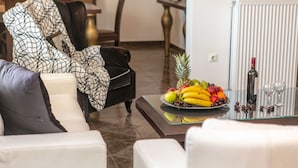 A modern living room with a sofa, a glass coffee table with fruit and wine, and a chair with a patterned throw. - Villa Agave (Naxos)