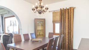 A dining area with a large table, chairs, a chandelier, a mirror, and a window with curtains. - Villa Agave (Naxos)