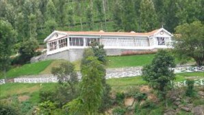 A large, two-story building with a symmetrical facade, surrounded by dense forest. - Mystique Ville (Ootacamund)
