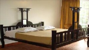 A single bed with a wooden frame and a mattress, a nightstand, and a window with curtains. - Mystique Ville (Ootacamund)