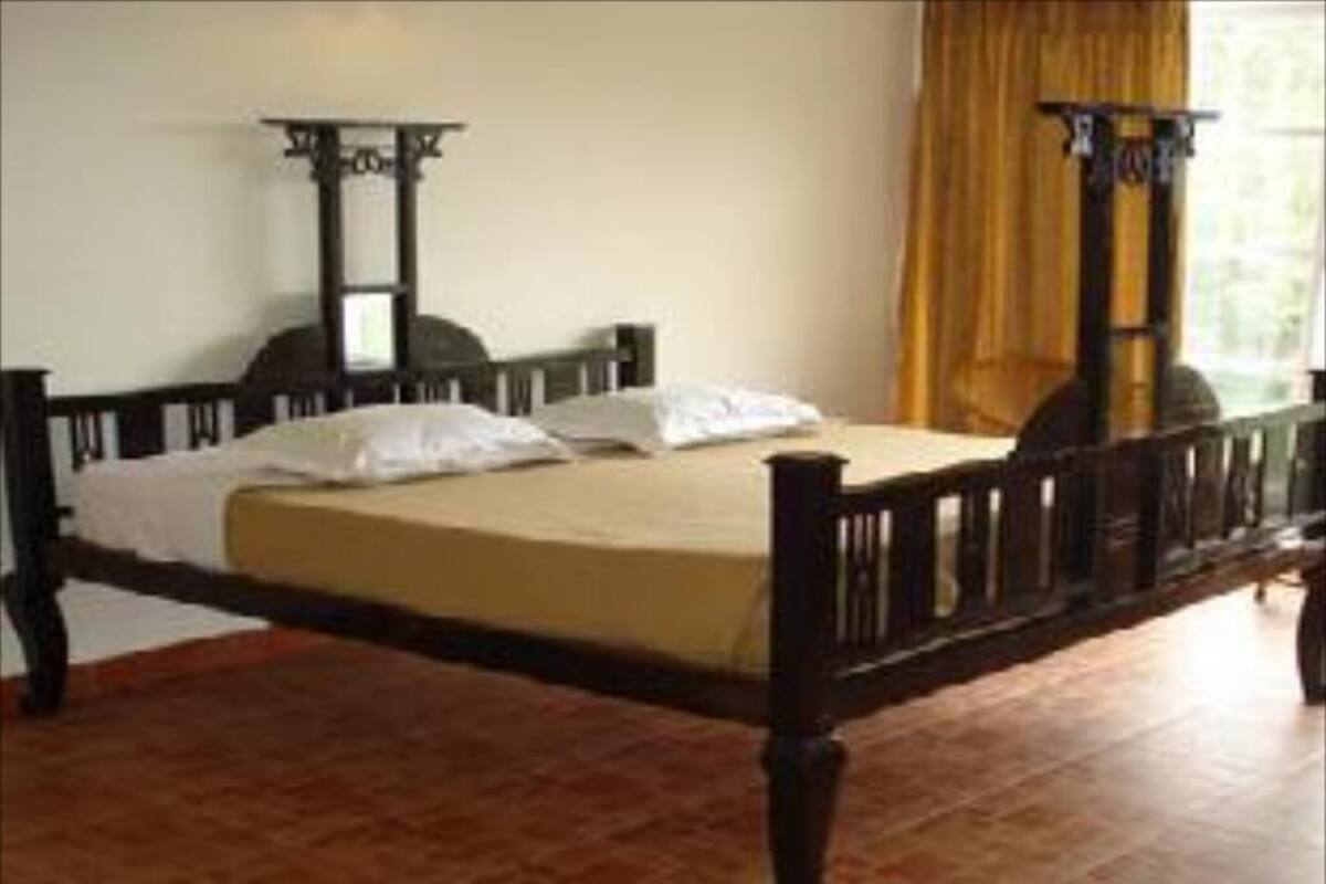 Una cama individual con estructura de madera y colchón, una mesita de noche y una ventana con cortinas.