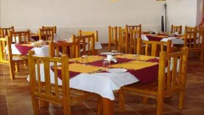 A dining area with wooden tables and chairs, covered with white tablecloths and red napkins. - Mystique Ville (Ootacamund)