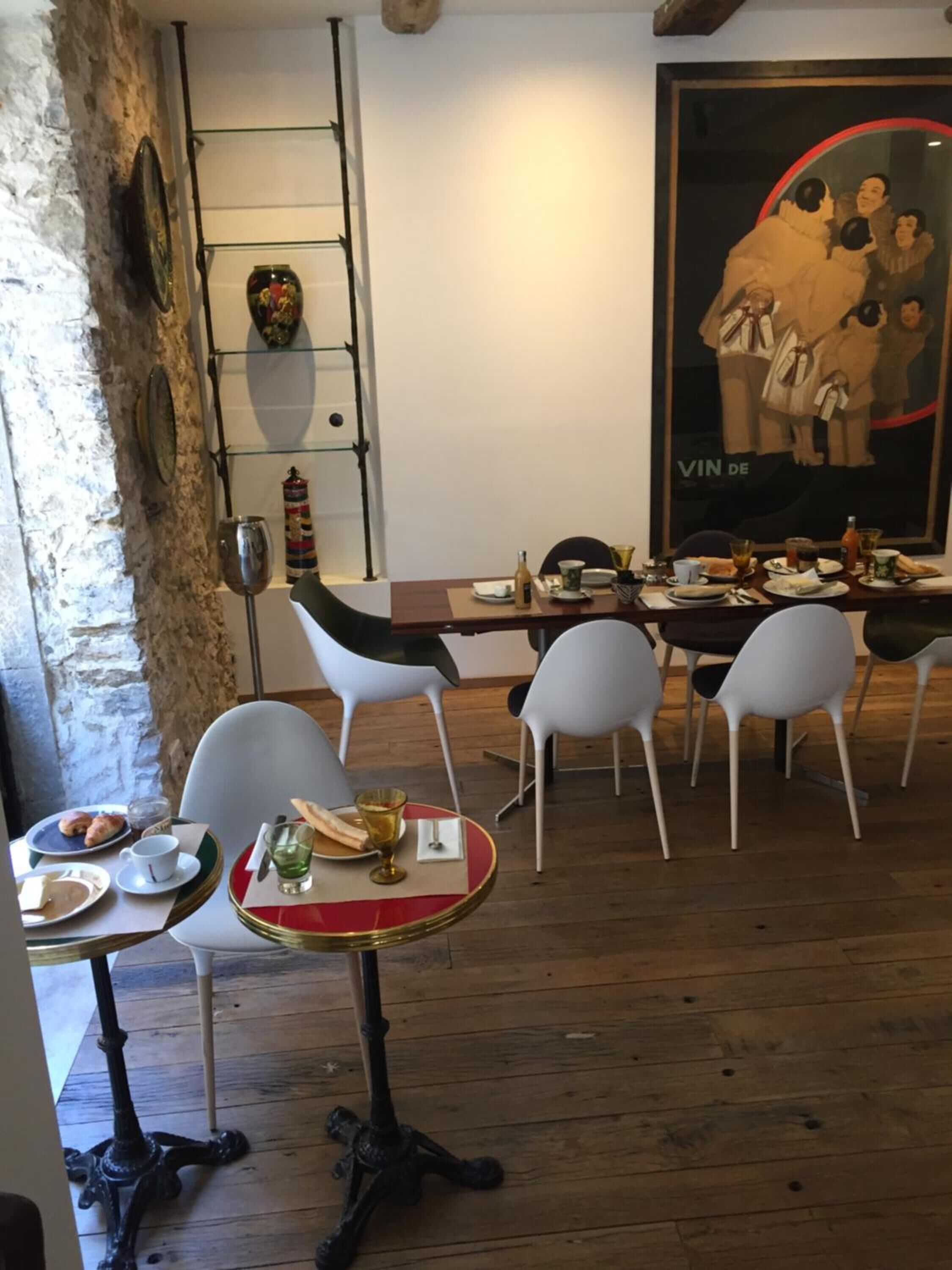 Un coin repas avec une table en bois dressée pour quatre personnes, entourée de chaises blanches. Une grande affiche avec un bordure rouge est accrochée au mur derrière la table.