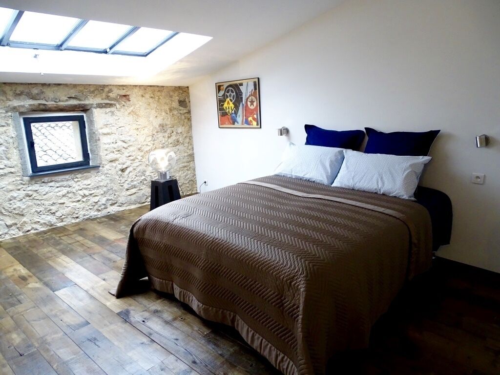 Une chambre avec un grand lit, une lucarne, un mur en pierre et une petite fenêtre.