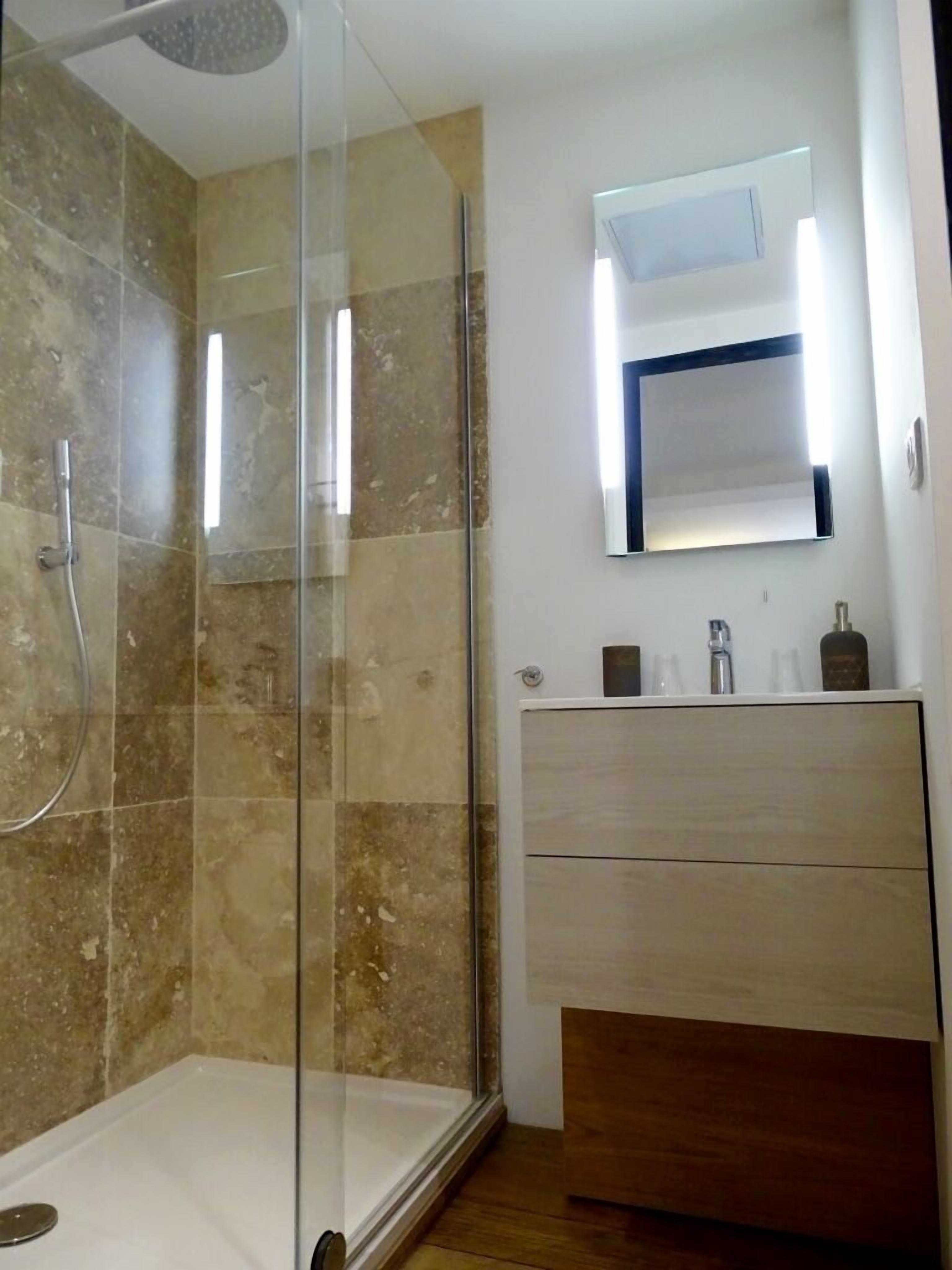 A modern bathroom with a glass-enclosed shower, a wooden vanity, and a mirror with integrated lighting.