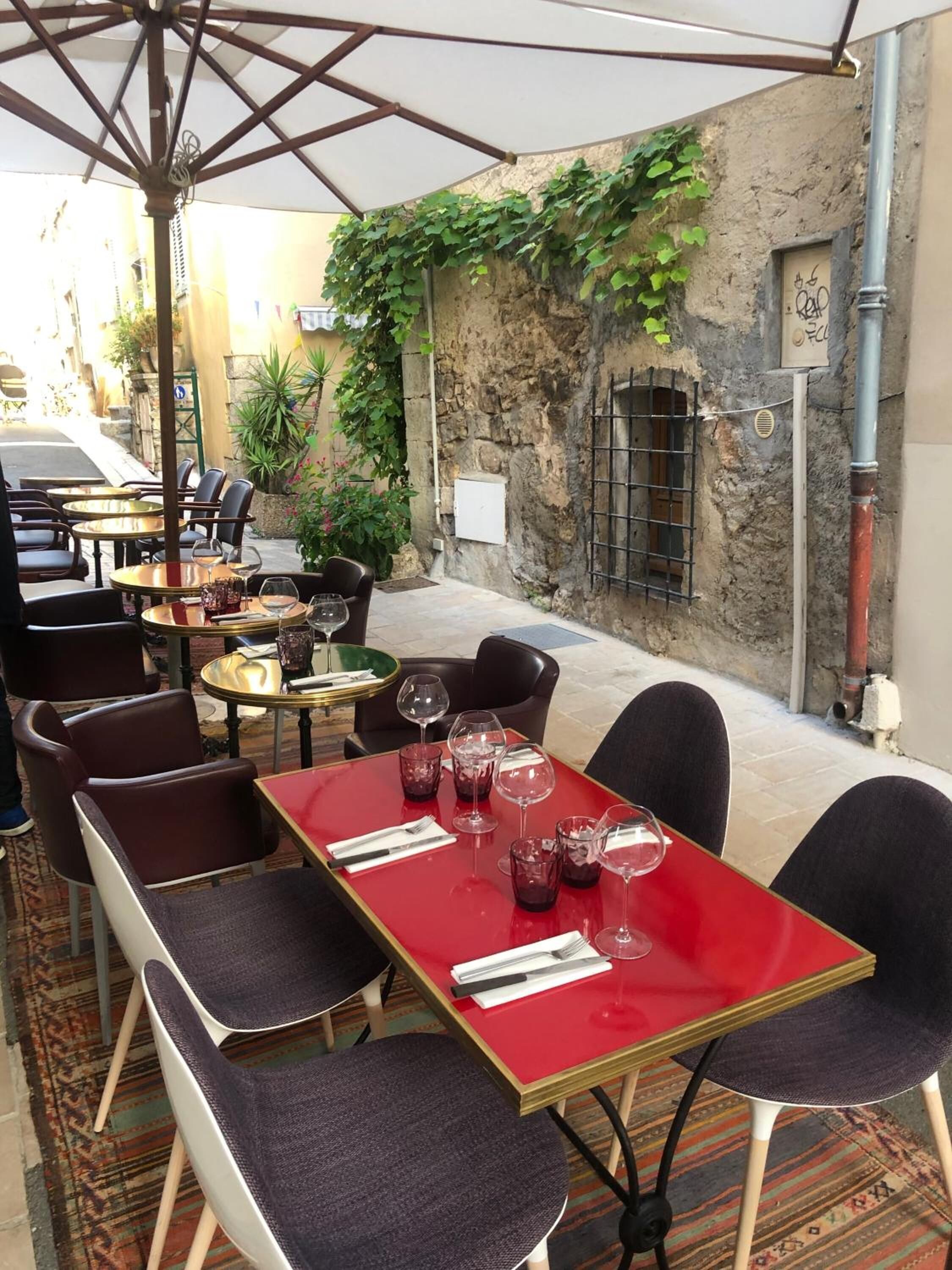 An outdoor café with tables and chairs, a red table, and a white umbrella.