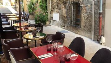 An outdoor café with tables and chairs, a red table, and a white umbrella.