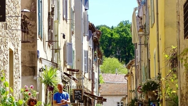 Una calle estrecha flanqueada por edificios, con mesas y sillas para exteriores y un café.