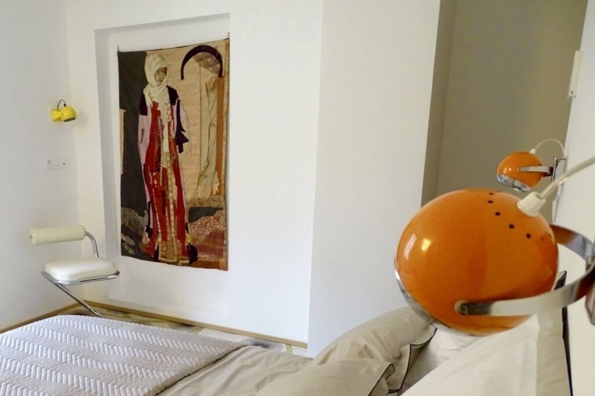 Ett modernt sovrum med en säng, en stol, en tavla och två sänglampor.