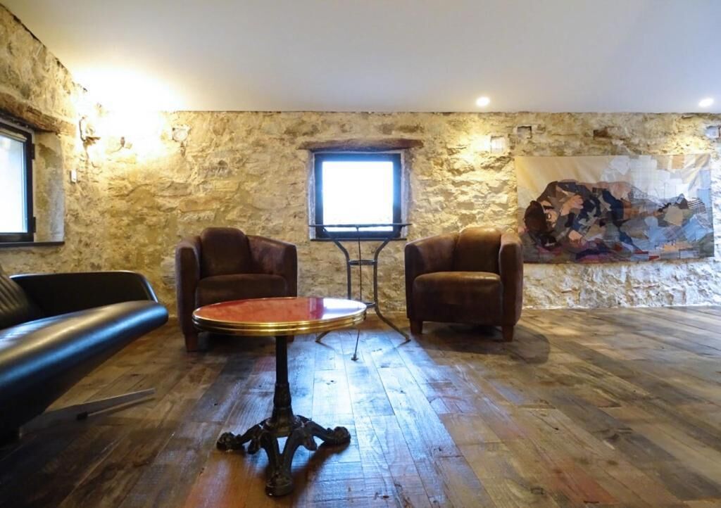 Une pièce avec un mur en pierre, une table ronde, deux fauteuils en cuir et une fenêtre.