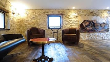 Une pièce avec un mur en pierre, une table ronde, deux fauteuils en cuir et une fenêtre.